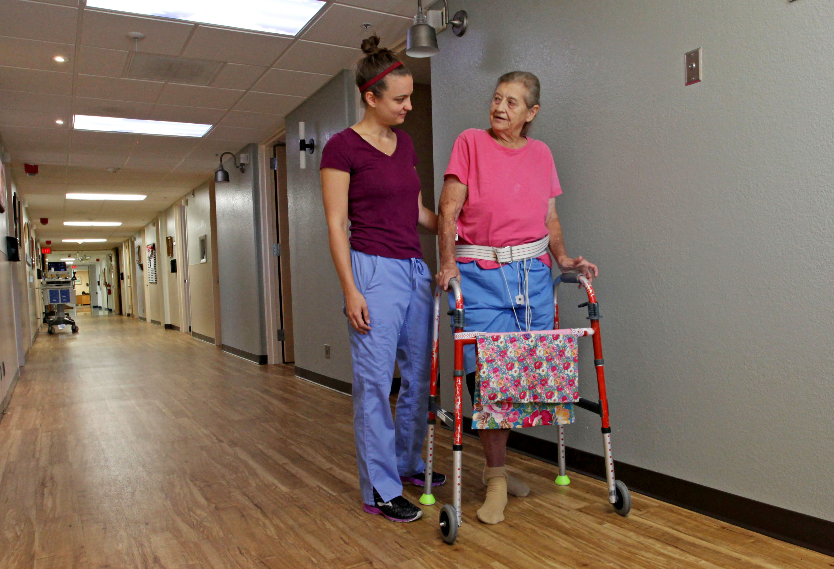 A caregiver helps an elderly patient walk with a walker